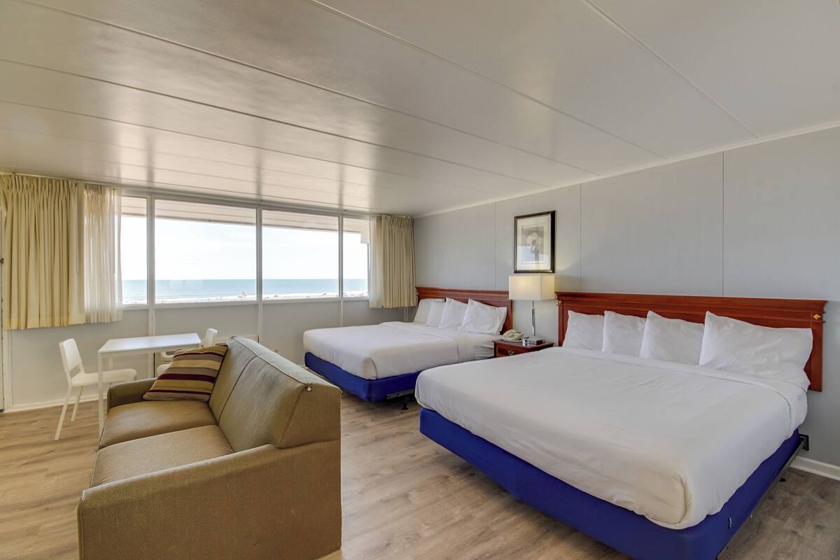 Une chambre d’hôtel avec deux lits, un canapé, un bureau et vue sur l’océan.