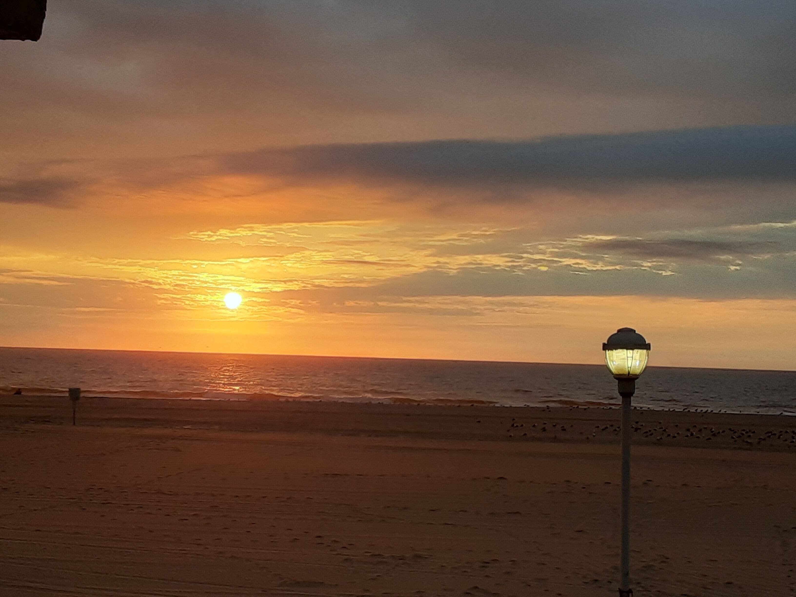 A sunset over a beach with a street lamp in the foreground.