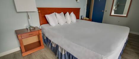 A neatly made bed with white linens and a wooden headboard, a bedside table with a lamp, and a blue door in the background.