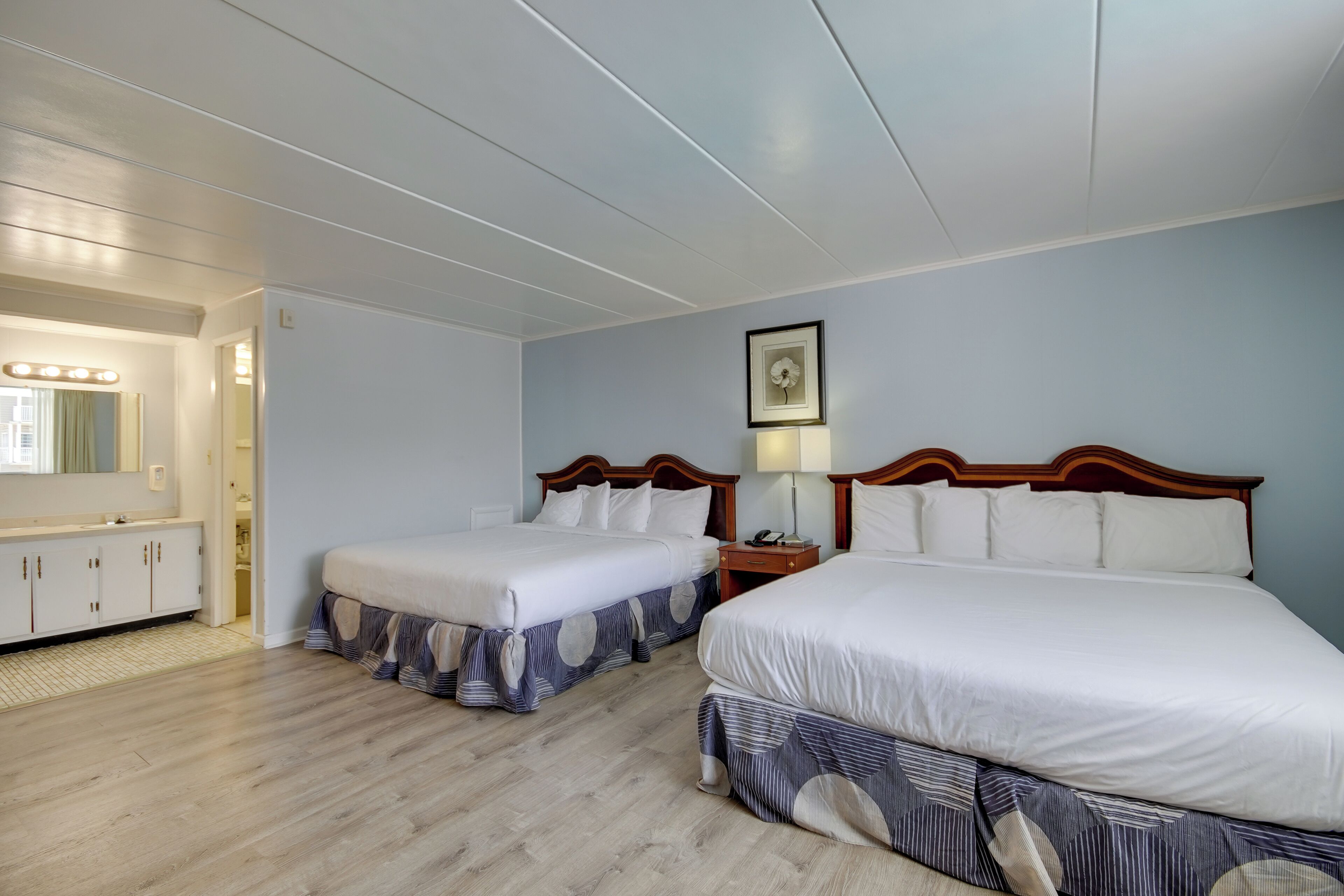 A hotel room with two beds, a vanity with a mirror, and a ceiling with recessed lighting.