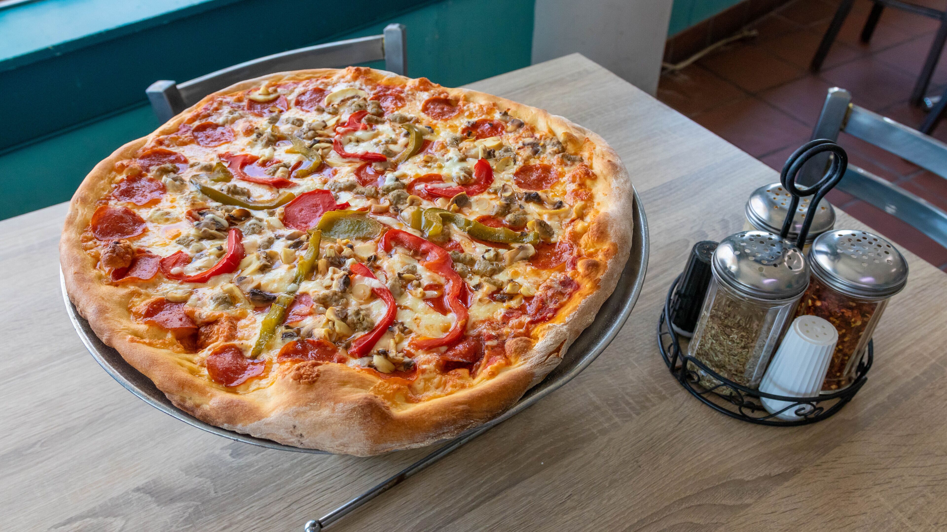 Une pizza garnie de divers ingrédients, servie sur un plateau en métal, accompagnée d’un moulin à poivre et d’un salier posés sur une table en bois.