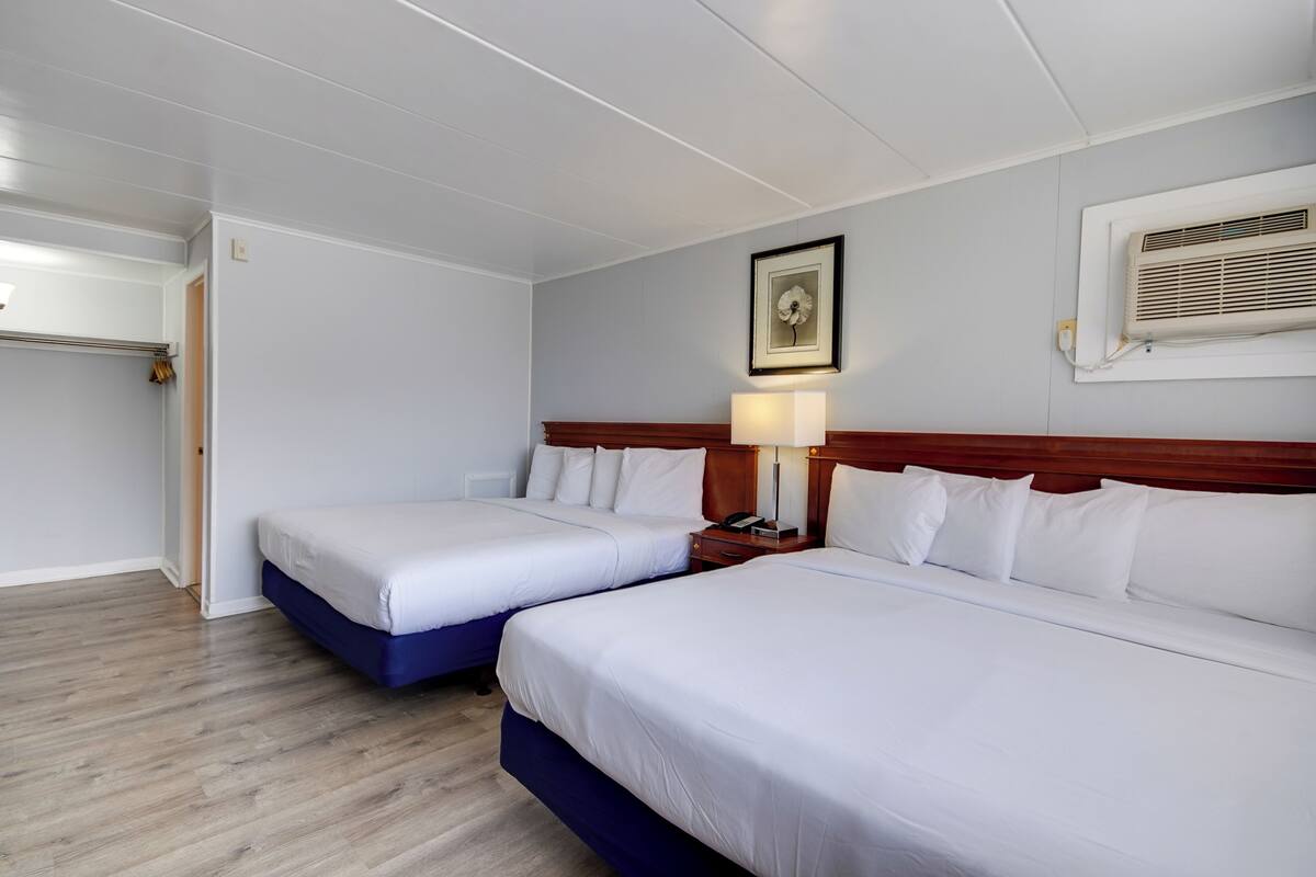 Une chambre d’hôtel avec deux lits, une tête de lit en bois, une table de chevet avec une lampe et un tableau encadré au mur.