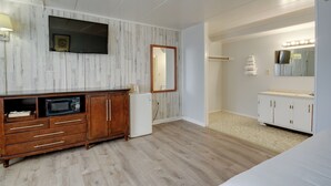 A bedroom with a wooden wardrobe, a flat-screen TV, a mirror with lights, and a bed.