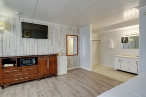 Un dormitorio con un armario de madera, un televisor de pantalla plana, un espejo con luces y una cama.