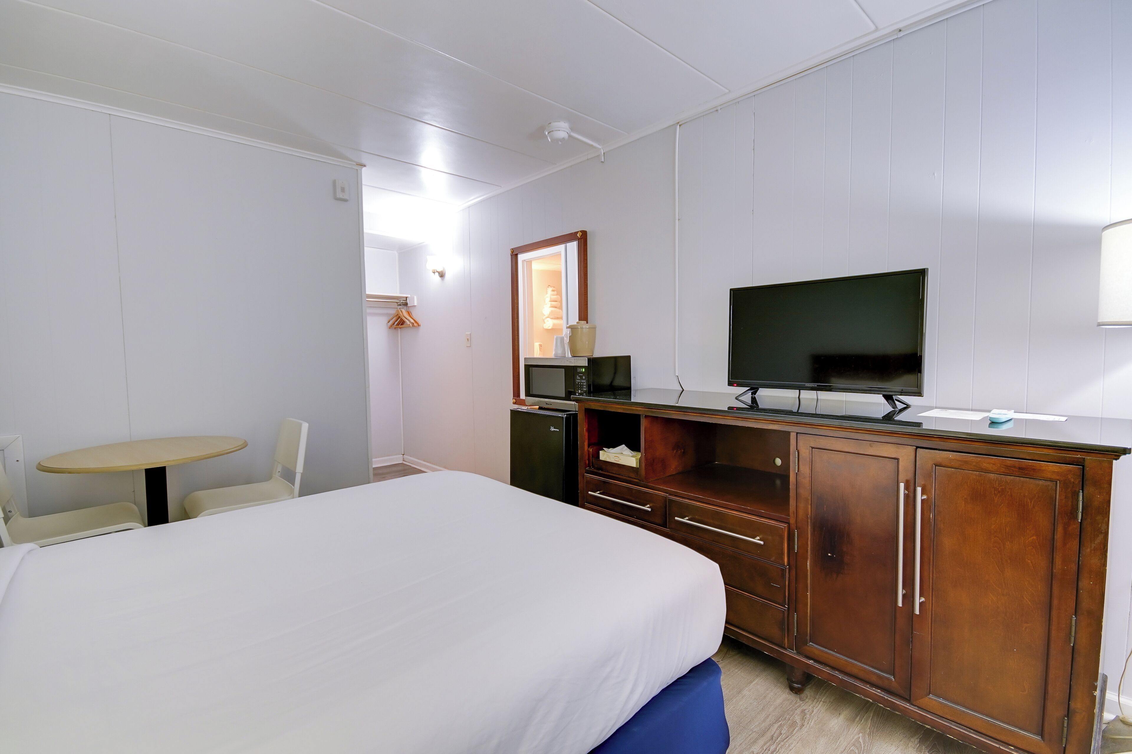 A hotel room with a bed, a wooden dresser, a television, a small table, and a chair.