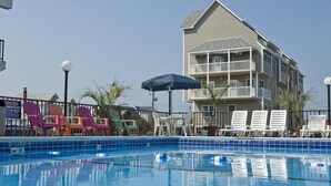 A swimming pool with lounge chairs and an umbrella, surrounded by a building with balconies.