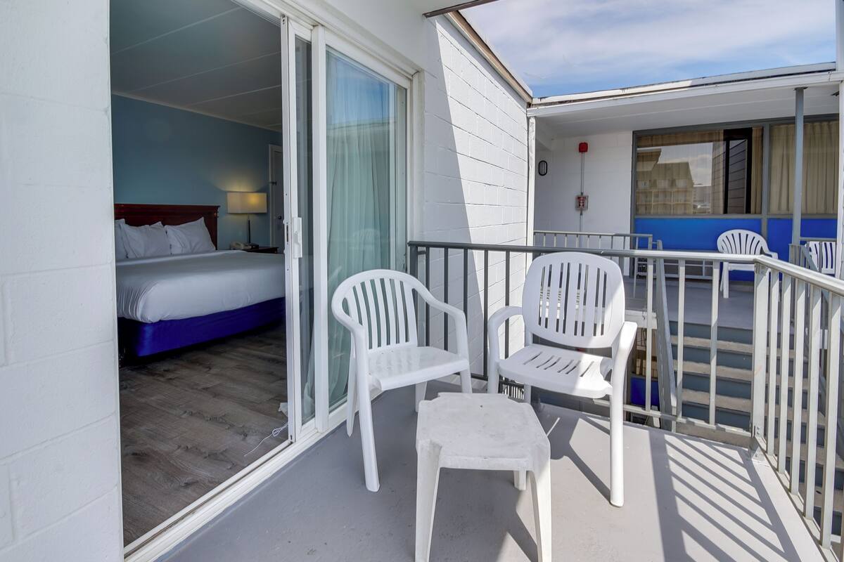 Un balcon avec des chaises en plastique blanches et un lit avec du linge de lit blanc.