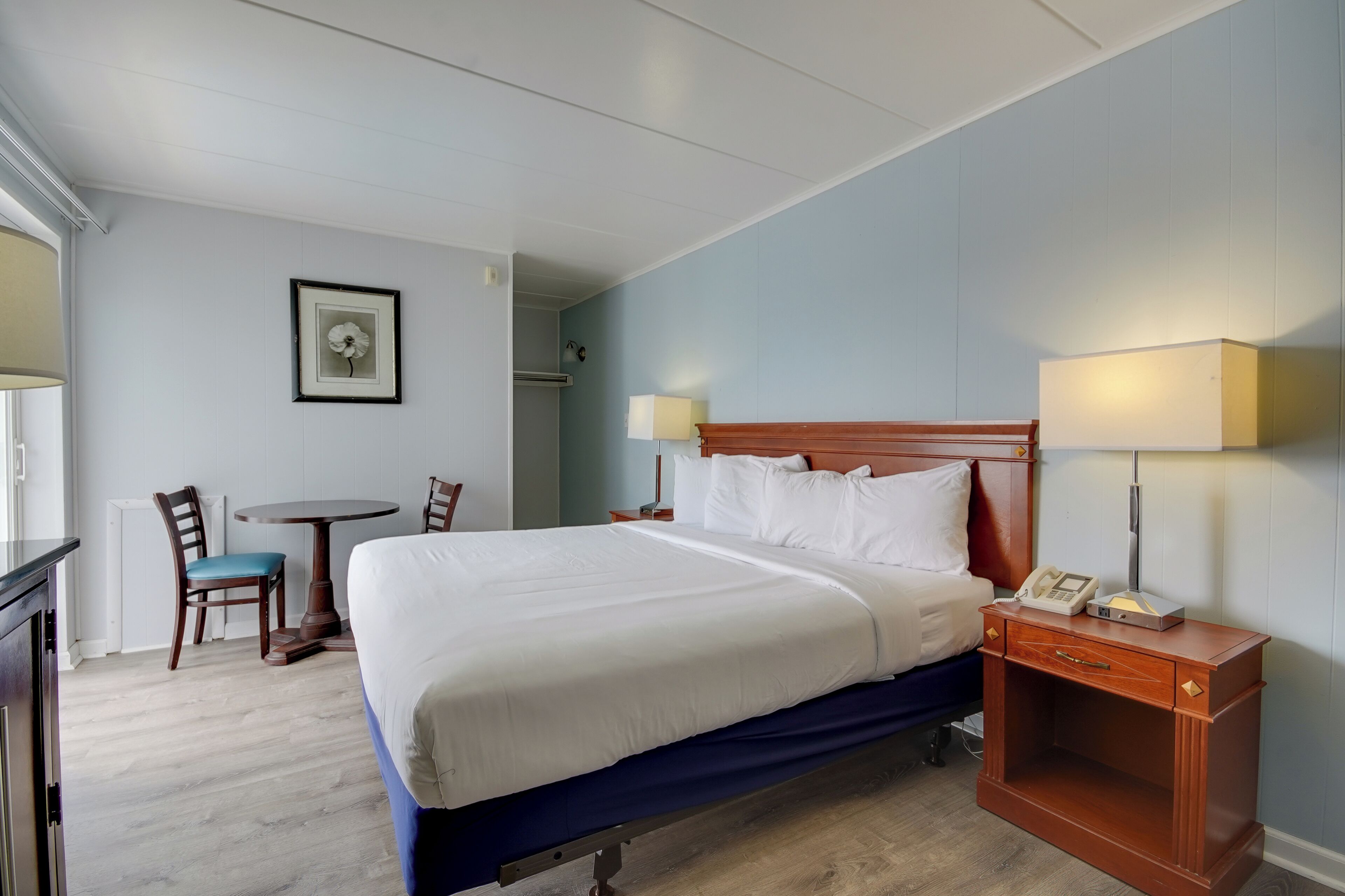 A hotel room with a large bed, bedside tables, a small table with chairs, and a framed picture on the wall.
