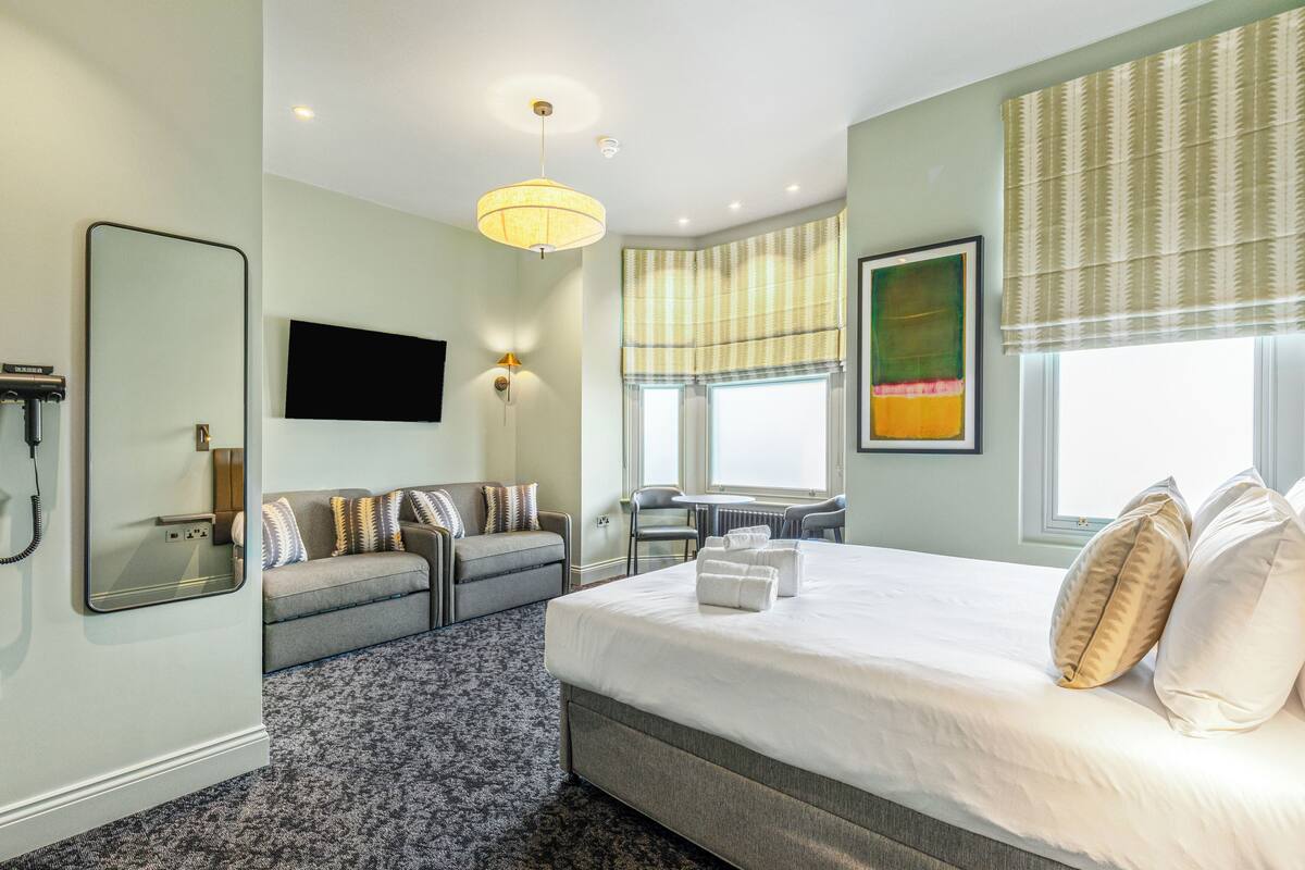 A hotel room with a large bed, a sofa, a desk, and a chair.