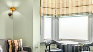 A room with a grey sofa, two chairs, a table, and a radiator. - Clapham Guest House (London)