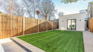 A backyard with a wooden fence, a well-maintained lawn, and a modern building with a glass door. - Clapham Guest House (London)