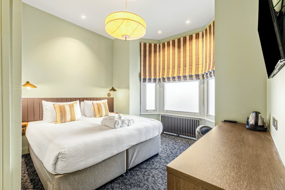 A hotel room with a large bed, bedside table, and a view of the outdoors through a window with curtains.