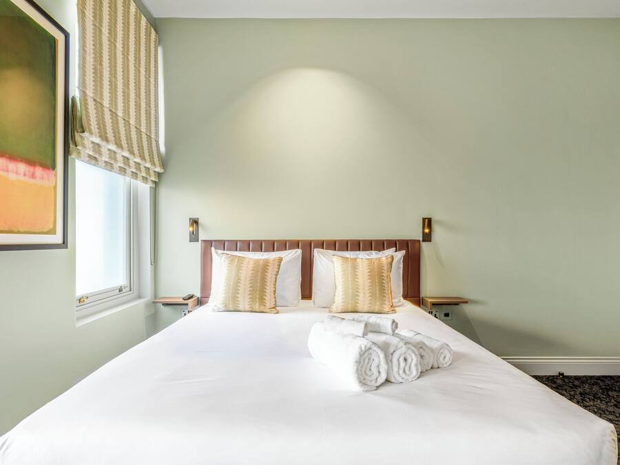 A hotel room with a large bed, two bedside tables, a headboard, and a window with a view.