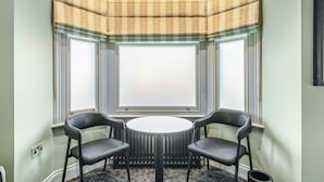 A corner room with a bay window, two chairs, a round table, and a radiator. - Clapham Guest House (London)