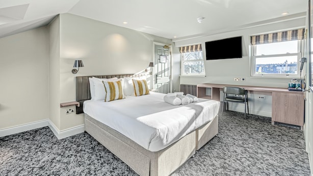 A modern hotel room with a large bed, a desk, and a view of the city. - Clapham Guest House (London)