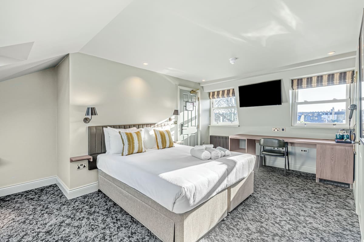 A modern hotel room with a large bed, a desk, and a view of the city.