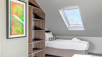 A bedroom with a sloped ceiling, a skylight, a bed with white bedding, and a wooden shelving unit.