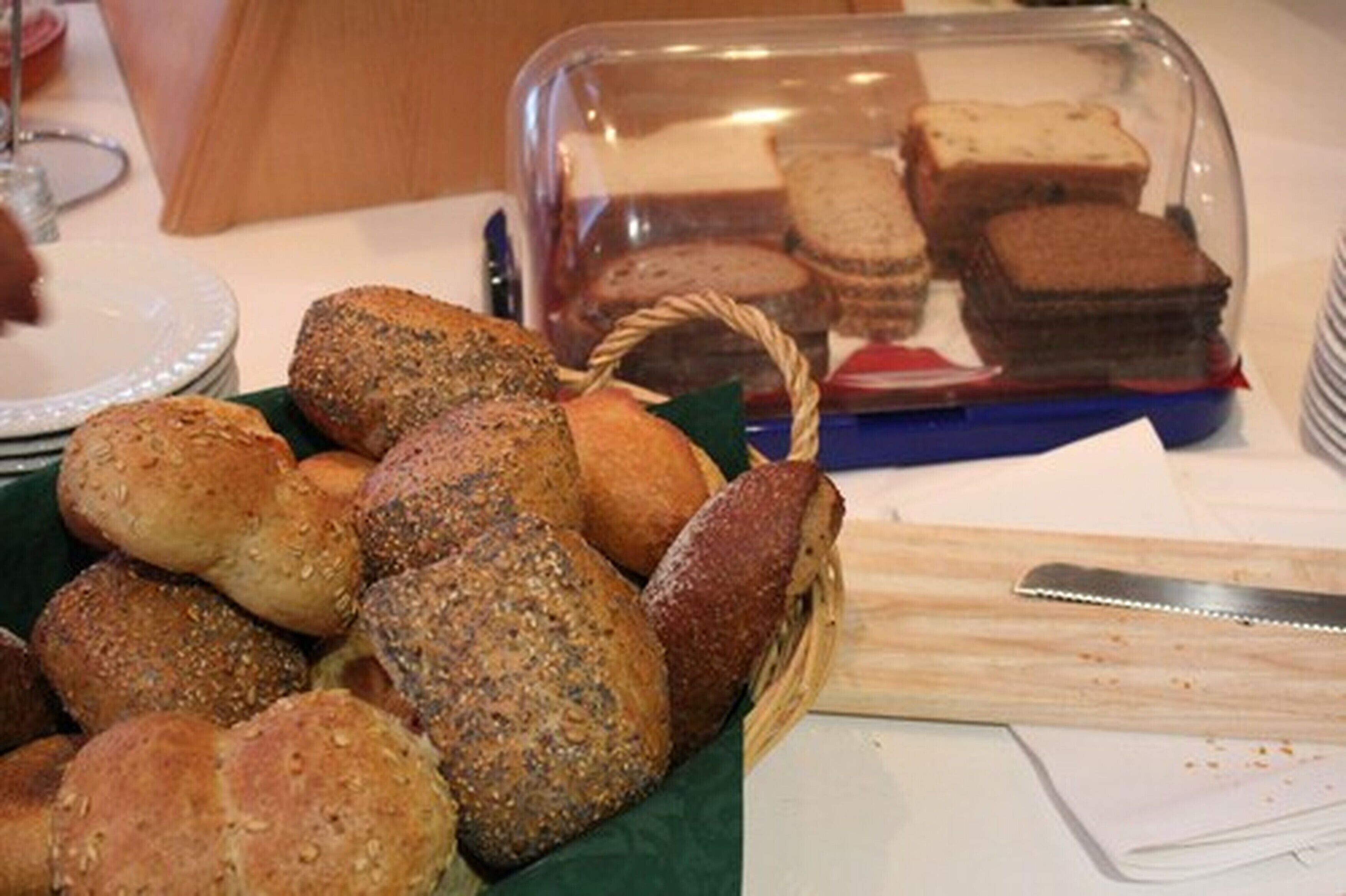 A variety of breads and pastries displayed on a table, with a clear plastic container in the background.