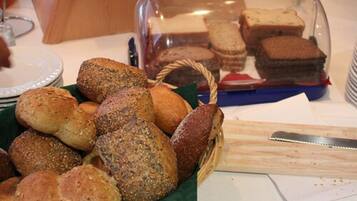 A variety of breads and pastries displayed on a table, with a clear plastic container in the background.