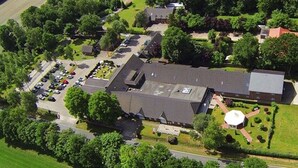 An aerial view of a large building complex with multiple parking lots, surrounded by greenery and trees.