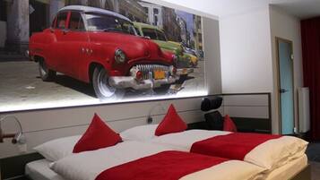 A hotel room with a large bed, red and white bedding, and a wall mural of vintage cars.