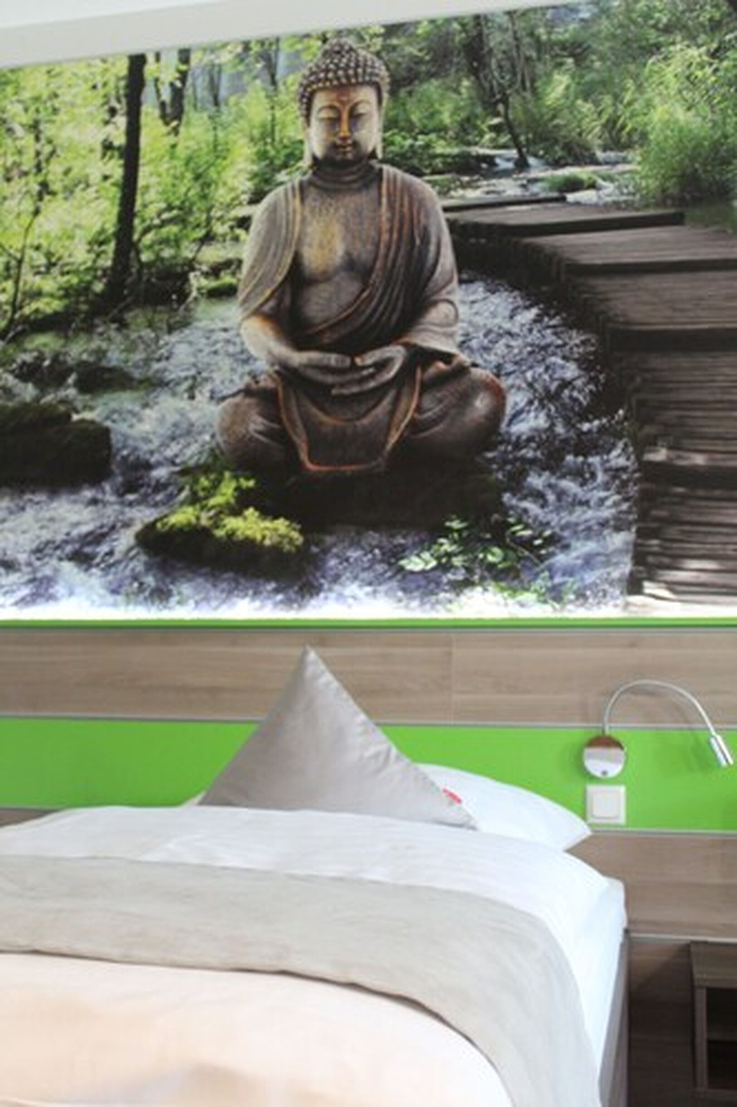 Een slaapkamer met een bed, een nachtkastje in het groen en een Boeddhabeeld aan de muur.