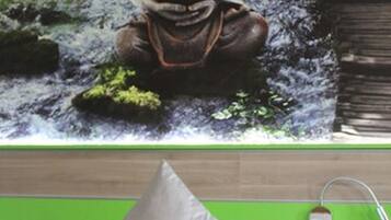 Een slaapkamer met een bed, een nachtkastje in het groen en een Boeddhabeeld aan de muur.