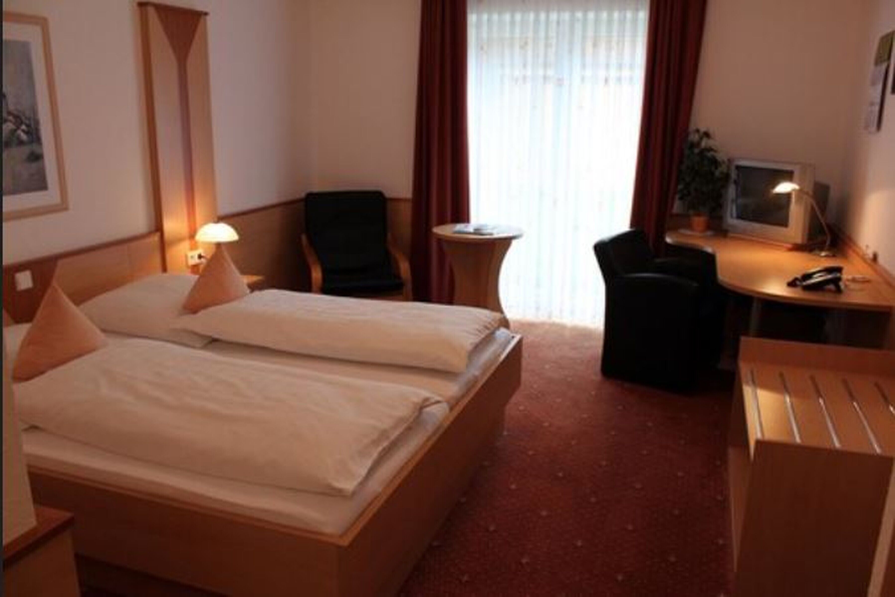 Quarto de hotel com duas camas, uma escrivaninha, uma cadeira, uma mesinha e uma televisão.