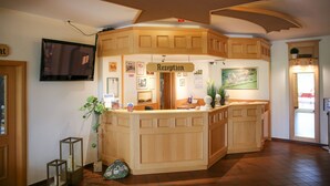A reception area with a wooden desk, a television mounted on the wall, framed pictures, and a sign that reads "Rezeption".