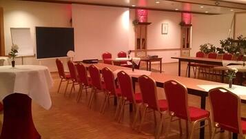 Ein Konferenzraum mit einem langen Tisch und roten Stühlen, weißen Tischen mit weißen Tischdecken sowie einer Projektionsleinwand.