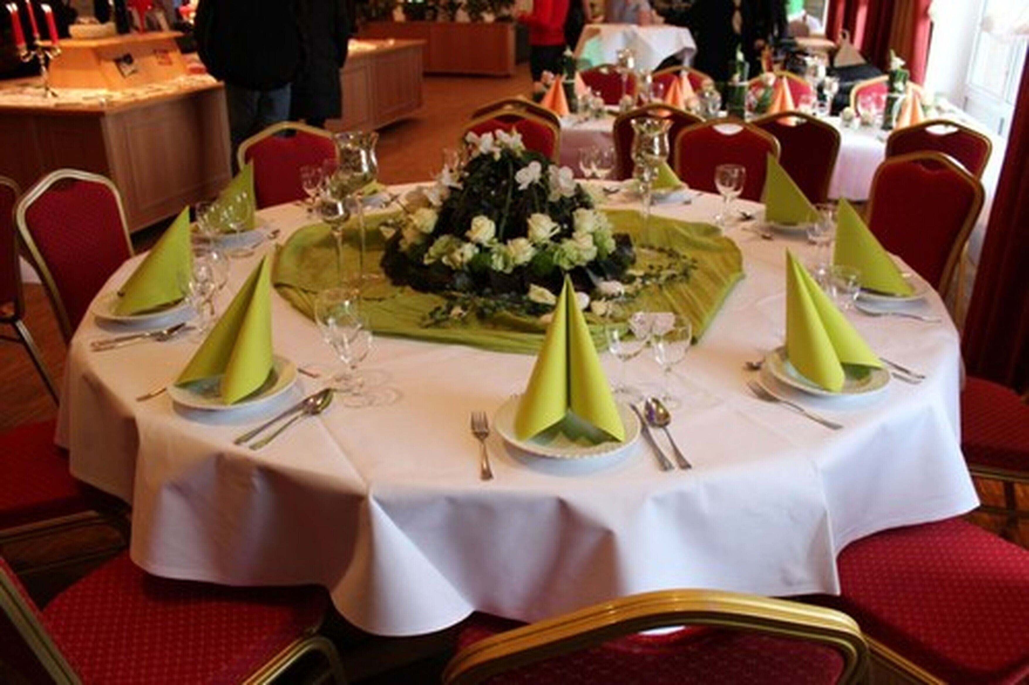 A round dining table with white tablecloth, green napkins, and a floral centerpiece.