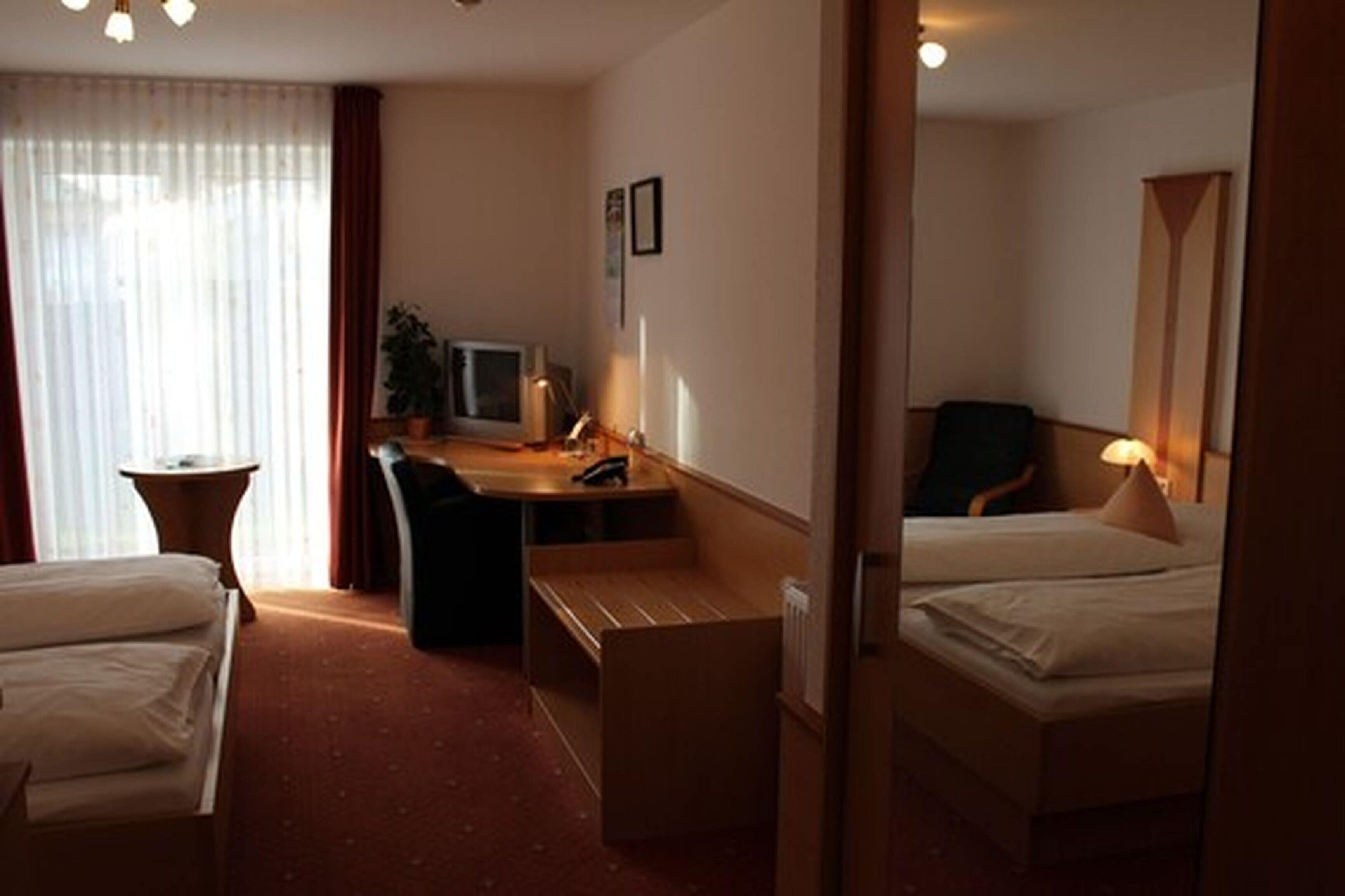 Habitació d'hotel amb dos llits, un escriptori, una cadira, un televisor i una làmpada.