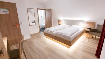 Ein modernes Hotelzimmer mit Holzboden, einem großen Bett mit weißer Bettwäsche, einem Schreibtisch mit Stuhl, einem kleinen Nachttisch und einem roten Vorhang.