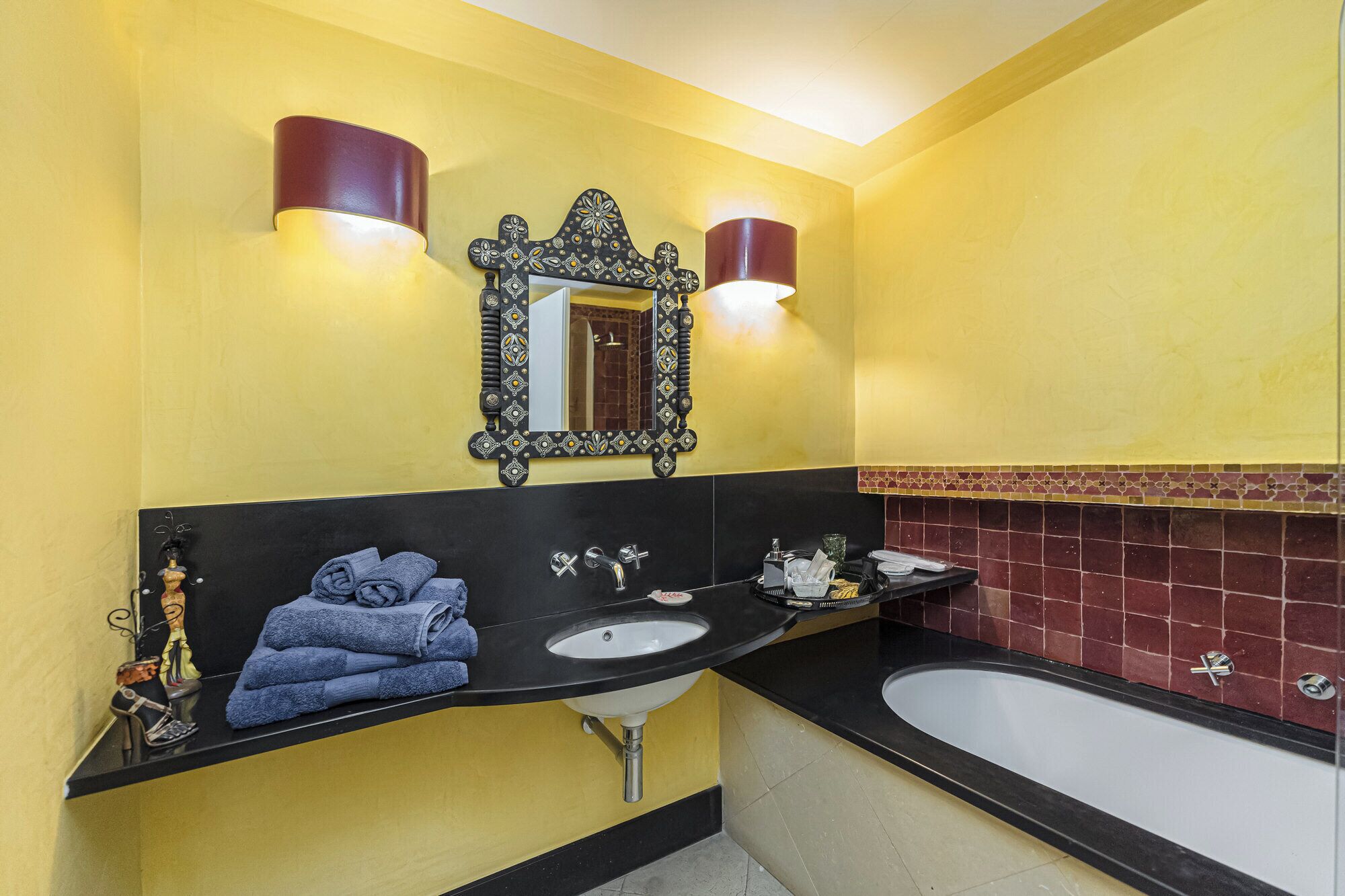 Un baño con encimera negra, un lavamanos y una bañera. Hay toallas apiladas en la encimera y un espejo decorativo sobre el lavamanos.