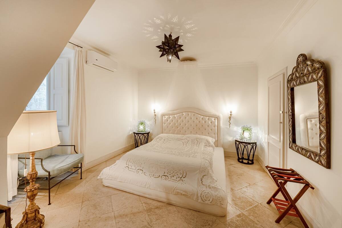 Une chambre à coucher comprenant un lit, des tables de chevet, une lampe, un miroir et un luminaire au plafond.