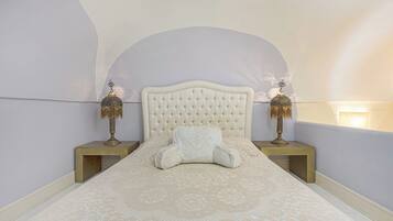 A bedroom with a tufted headboard, a patterned bedspread, two bedside tables with lamps, and a wall-mounted light.