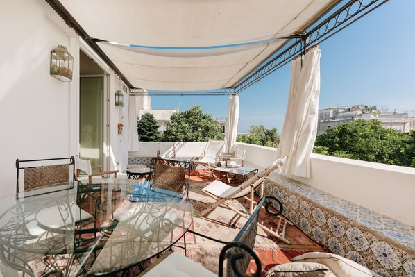 A balcony with a glass table, chairs, and a view of the city.