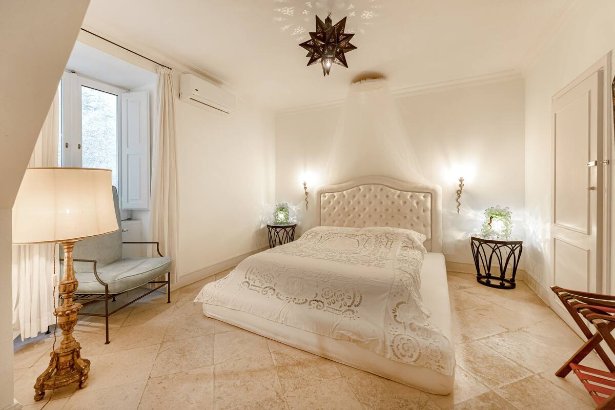 Une chambre à coucher comprenant un lit, une table de chevet, une lampe, une chaise et un luminaire décoratif au plafond.