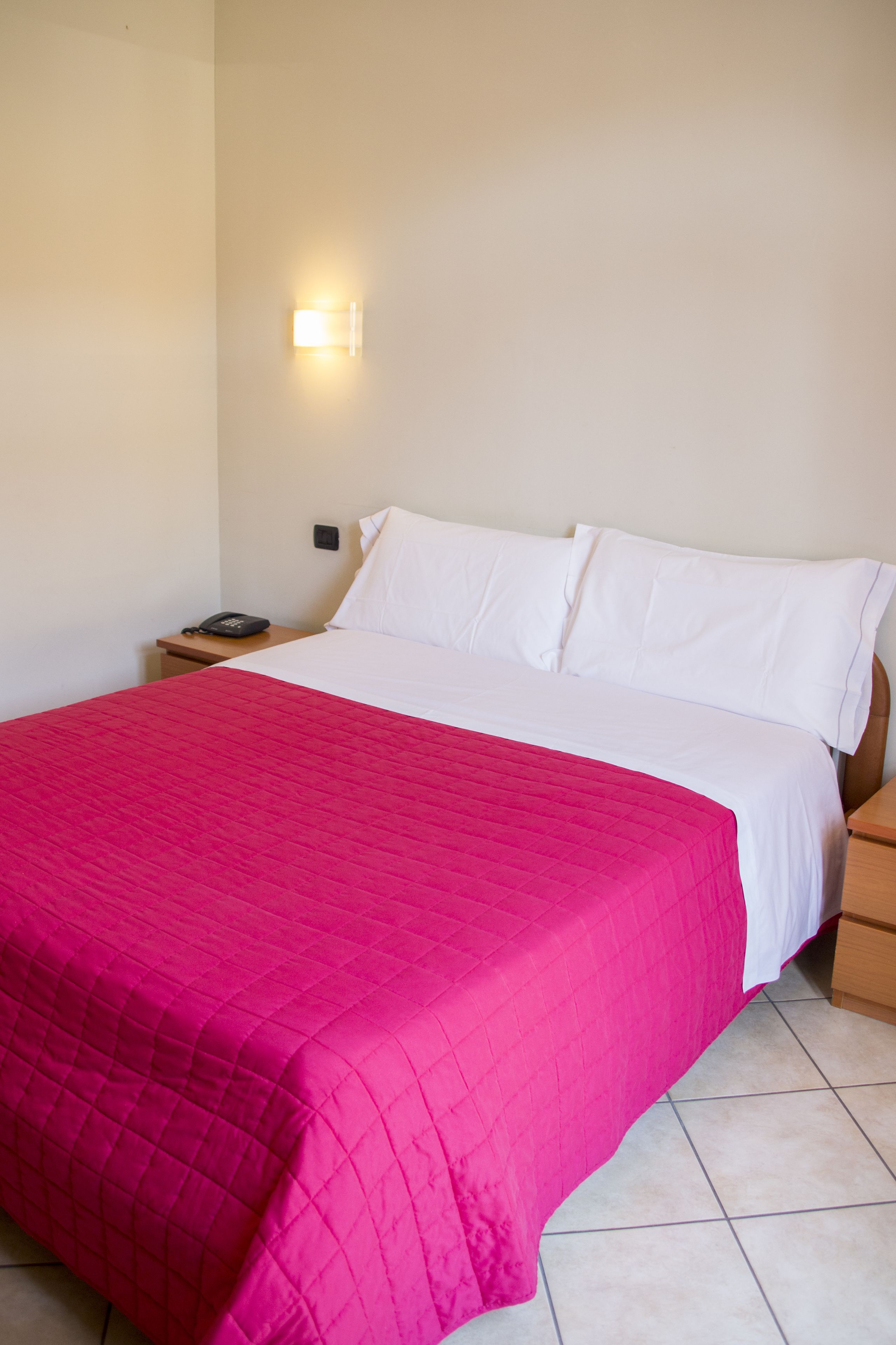 Una habitación de hotel con cama, mesita de noche y lámpara de pared.