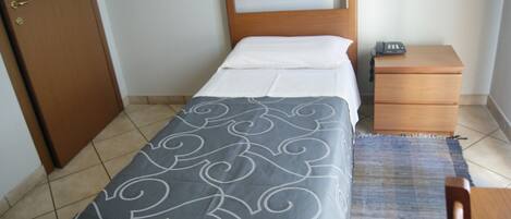A small, neatly arranged bedroom with a bed, bedside table, and a nightstand.