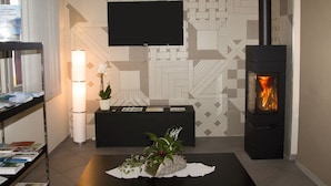 A modern living room with a fireplace, a flat-screen TV, and a decorative plant arrangement. - Hotel Parini (Bosisio Parini)