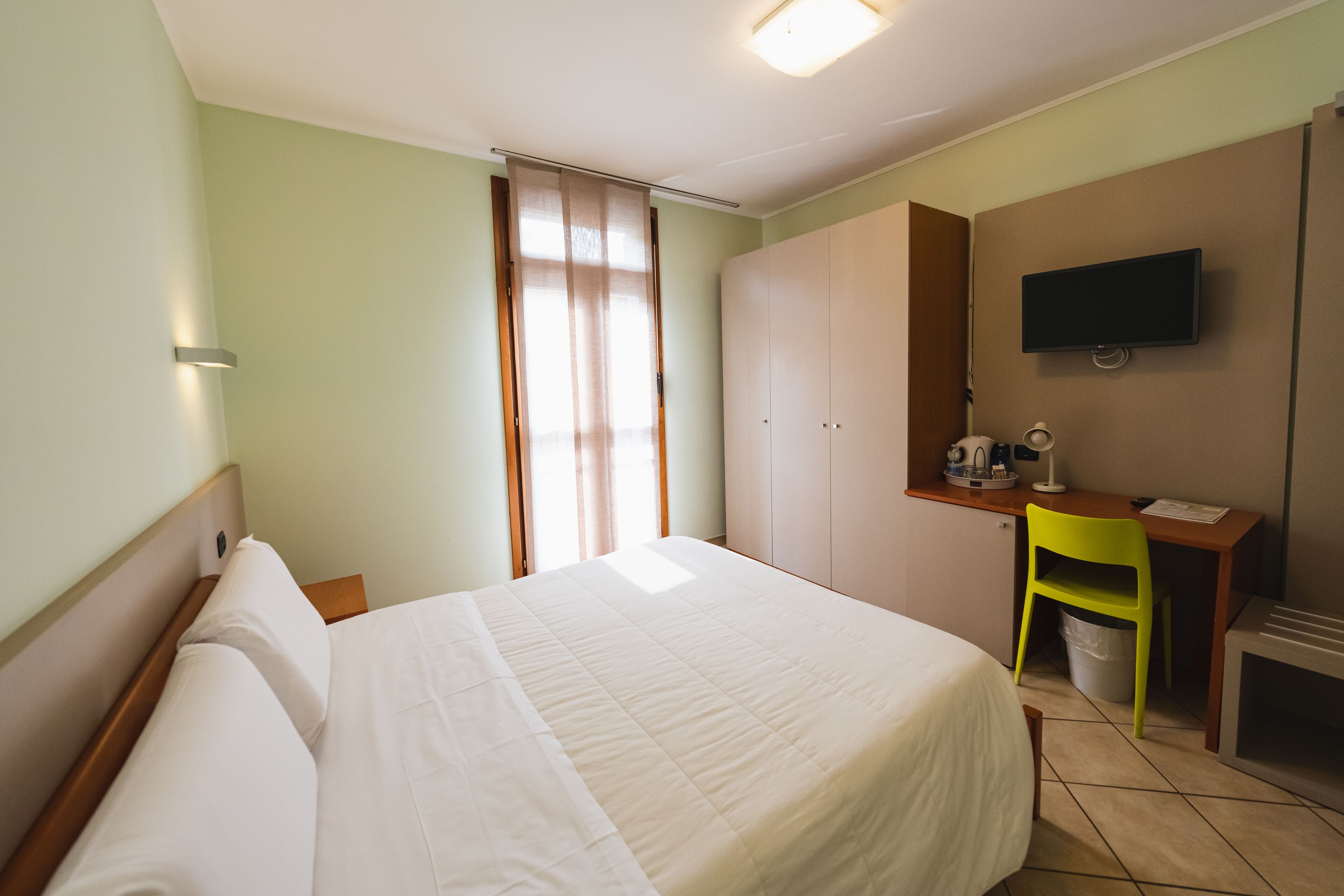 Ett hotellrum med en säng, ett skrivbord med en stol, en tv och en garderob.