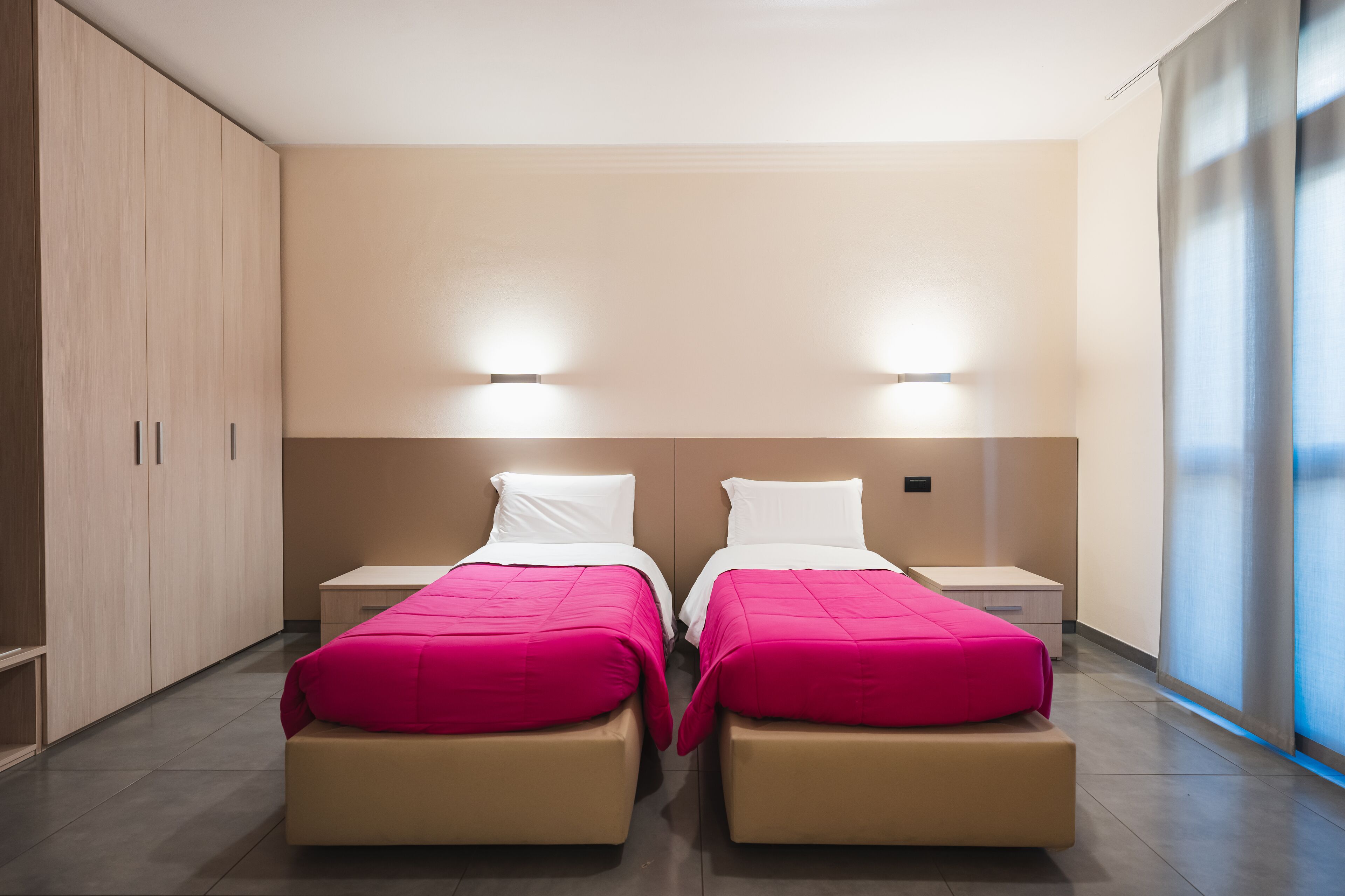 Una habitación de hotel moderna con dos camas, un armario amplio y un ventanal luminoso.
