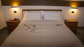 Una cama bien tendida con una colcha blanca y almohadas, dos mesitas de noche con lámparas y un cabecero de madera.