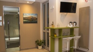 A modern hotel lobby with a glass door entrance, a green reception desk, white bar stools, a flat-screen TV, and a painting of a mountain landscape. - Hotel Parini (Bosisio Parini)