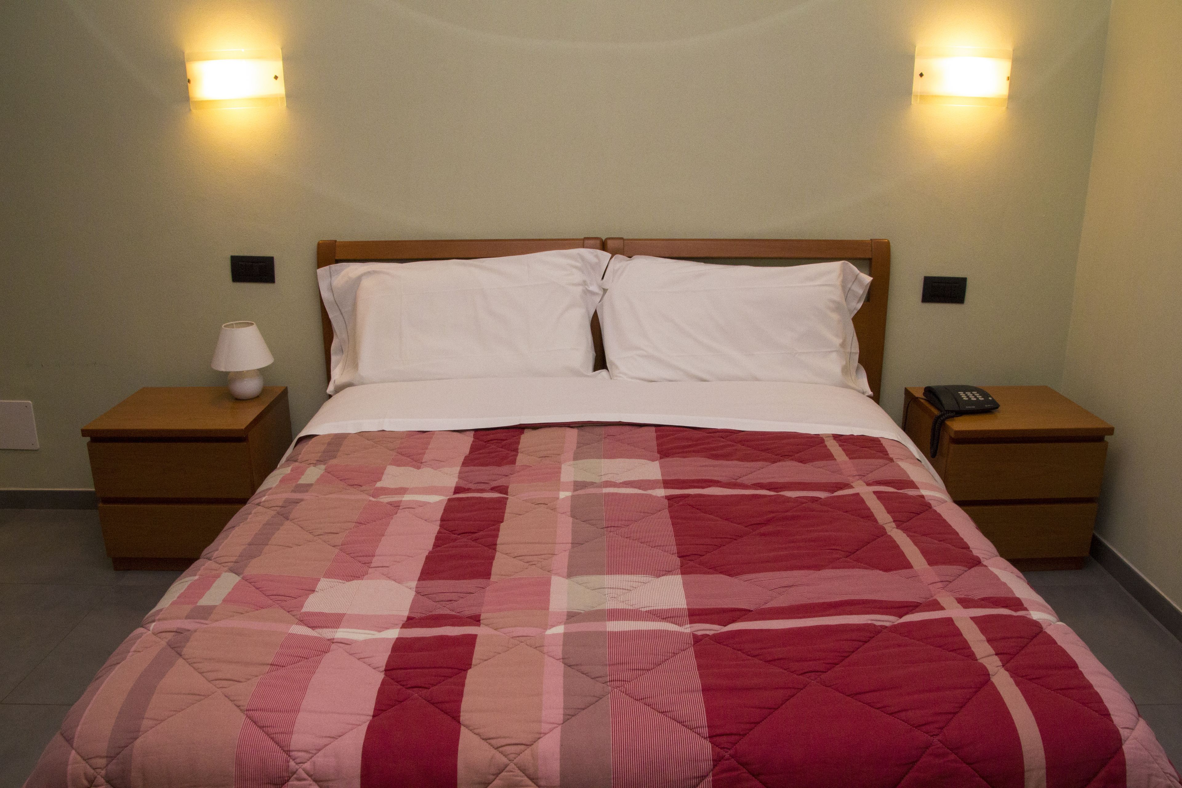 Un letto rifatto con una coperta a quadri rossi e bianchi, due comodini con lampade e applique.