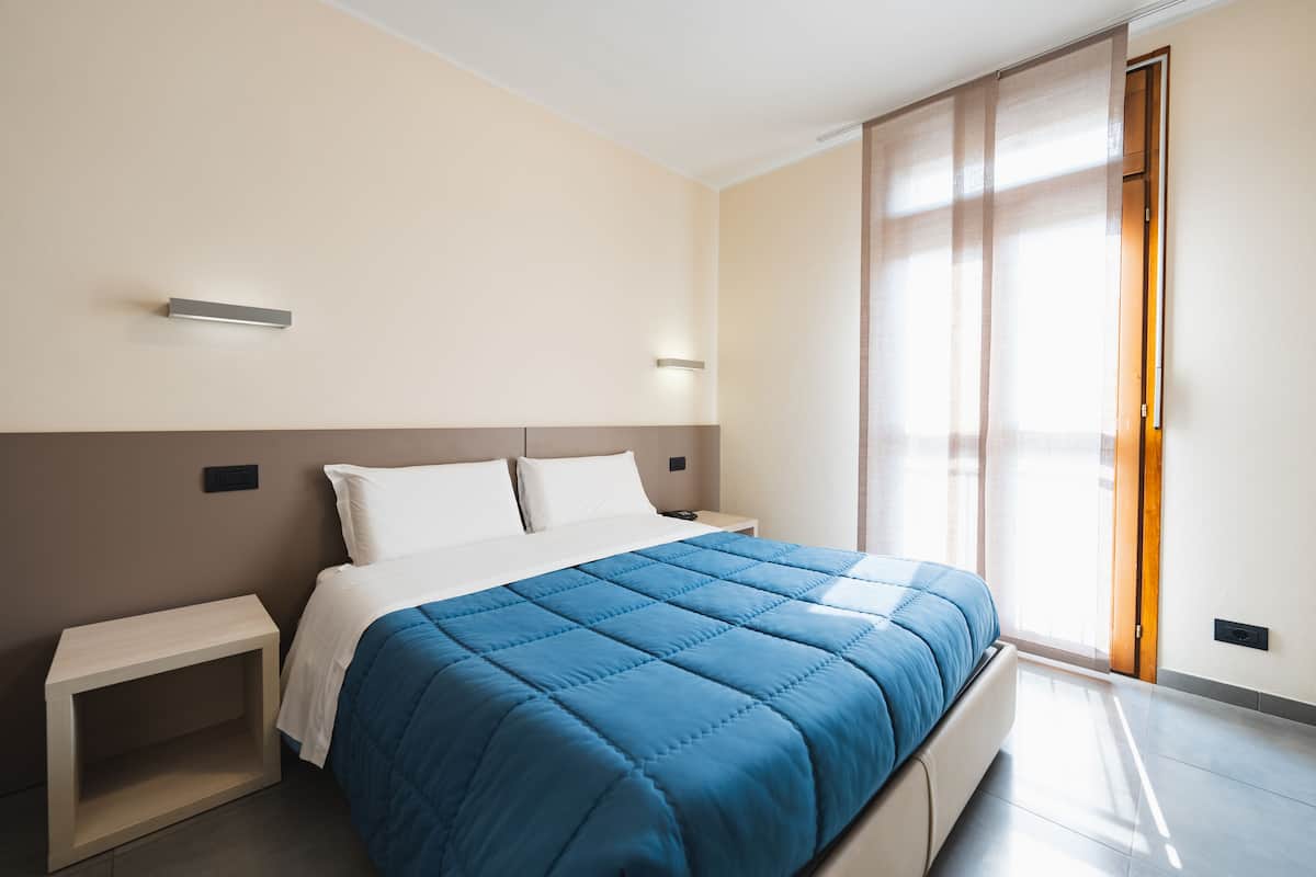 A modern bedroom with a large bed, a bedside table, and a sliding door to a balcony.