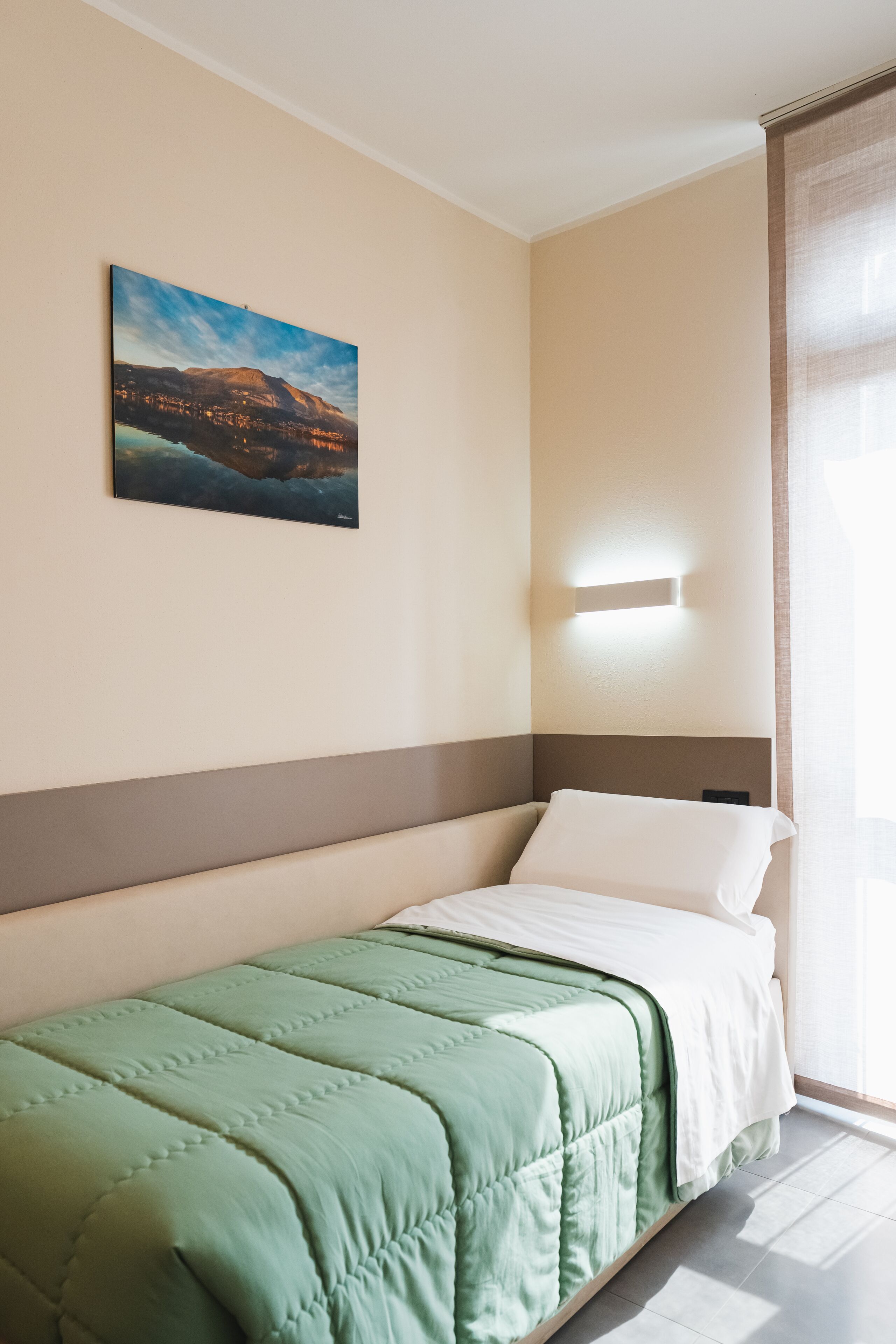 Habitación de hotel con una cama individual, un cuadro en la pared y una ventana con cortinas.