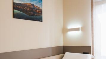 Habitación de hotel con una cama individual, un cuadro en la pared y una ventana con cortinas.