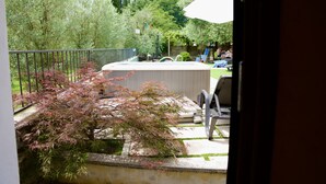 Un patio trasero con un jacuzzi, un porche con sillas y vistas a árboles y césped.